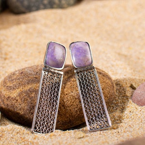 Può includere: Un paio di orecchini d'argento con un delicato design a catena e una pietra preziosa viola al centro di ogni orecchino.