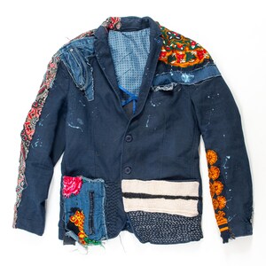 Peut inclure: Un blazer bleu marine avec des détails patchwork. La veste présente des patchs en denim, floraux et à motifs. Des éclaboussures de peinture blanche ajoutent une touche unique. Les manches ont des accents en tissu décoratifs. Le blazer a deux boutons et un revers cranté.