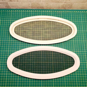 May include: Two white, oval-shaped frames with a mesh insert, likely for a window or vent. The frames are set against a green cutting mat with grid lines. The mesh is a light tan color.