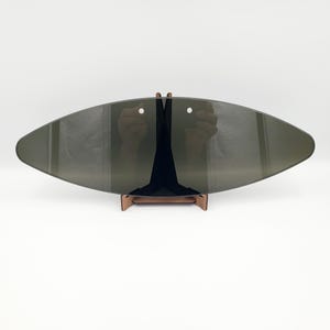 May include: A grey, oval decorative object with two holes, mounted on a brown wooden stand. The object has a dark tint and a smooth surface. The stand is made of thin, angled pieces of wood.