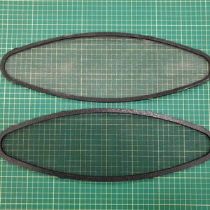 May include: Two black oval-shaped mesh screens with a dark border. The screens are set against a green grid background. The mesh is a light beige color.