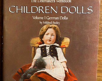 Pode incluir: Capa do livro "Children Dolls: Volume I German Dolls" de Mildred Seeley. A capa apresenta uma ilustração colorida de uma boneca vestindo um vestido vermelho e branco, sentada em uma cadeira de madeira. A boneca tem cabelo loiro e olhos azuis. O título do livro está em letras grandes e em negrito.