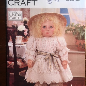 Puede incluir: Un patrón de muñeca vintage Vogue para una muñeca que lleva un vestido de encaje blanco, un sombrero de paja y zapatos blancos. El patrón incluye una transferencia de hierro a todo color para la cara.