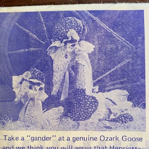 May include: Two handmade dolls dressed in white with floral patterns. The dolls are wearing bonnets and are sitting on a blue background. The dolls are made in the style of a vintage Ozark Goose doll.