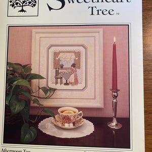 May include: A cross-stitch pattern for a needlepoint project titled "Afternoon Tea" featuring a woman sitting at a table by a window. The pattern is from The Sweetheart Tree, a cross-stitch design company.