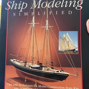 May include: A book cover titled "Ship Modeling Simplified" featuring a detailed model sailboat. The cover has a red border and includes text about model construction and an Italian-English dictionary of nautical terms. The author's name is Frank Mastini.