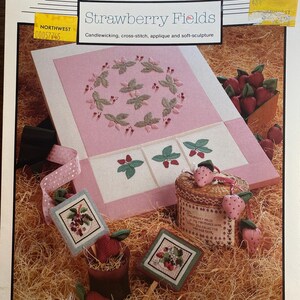 May include: A craft pattern titled "Strawberry Fields" by Silver Threads. The design features cross-stitch and applique strawberry motifs. The image includes a pink and white stitched piece, a basket, and decorative strawberry accents.