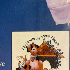May include: A cartoon dog sitting in front of a dog house with the text "My House Is Your House" and "Dog House" on the house. The dog is brown and black with a white collar and a tag that says "28".