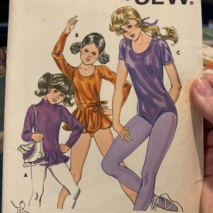 May include: Vintage Kwik Sew sewing pattern 1214 featuring illustrations of girls in dance or skating outfits. The pattern includes sizes 8-14. The cover art shows three girls in purple and orange leotards and leggings. Designed by Kerstin Martensson.