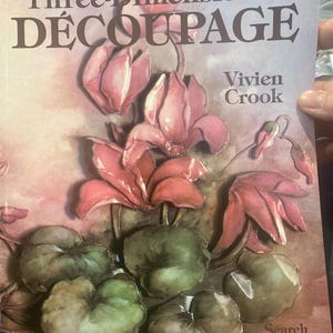 May include: A book cover titled "Three-Dimensional DÉCOUPAGE" by Vivien Crook. The cover features a watercolor illustration of pink flowers and green leaves. The book is published by Search Press.