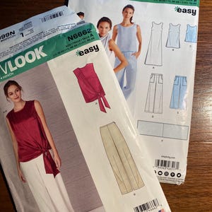 May include: Two sewing patterns for women's clothing. The pattern on the left is for a red top with a tie at the waist and white pants. The pattern on the right is for a blue dress, a white dress, a blue top, and white pants. Both patterns are from New Look and are labeled "easy".