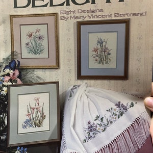 May include: A book titled "Day's Delight" with eight cross stitch designs by Mary Vincent Bertrand. The book cover features three framed cross stitch patterns of flowers, a white crocheted shawl with a floral design, and the text "Book 7".