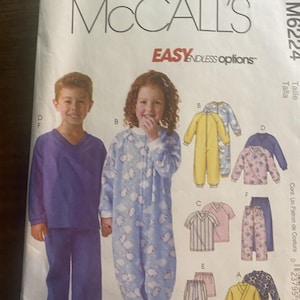 May include: A McCall's M6224 sewing pattern envelope featuring illustrations of children's sleepwear. The front shows a purple V-neck pajama set and a light blue one-piece sleeper with a cloud print, alongside various other pajama styles.