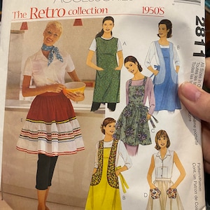 Op de afbeelding: Een vintage naaipatroon voor schorten uit de jaren 1950. Het patroon bevat vier verschillende schortenstijlen, elk met een ander ontwerp en kleur. Het patroon is van McCall's Fashion Accessories.