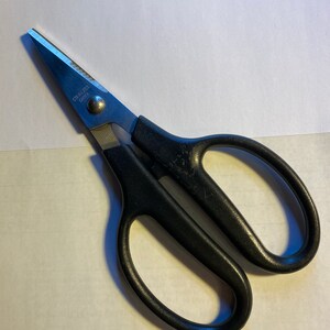 May include: Black handled kitchen shears with stainless steel blades. The blades have a serrated edge. The shears are labeled "Stainless Steel China".