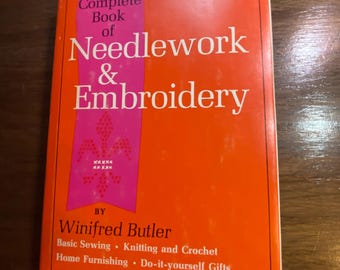 May include: An orange book titled "The Complete Book of Needlework & Embroidery" by Winifred Butler. The book features a pink vertical stripe with text and a decorative pattern. Additional text includes "Basic Sewing, Knitting and Crochet, Home Furnishing, Do-it-yourself Gifts."