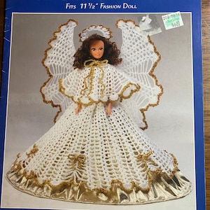 May include: A crochet pattern for an Angel Gloria Fashion Doll. The doll is wearing a white dress with gold trim and large white wings. The pattern fits a 11 1/2 inch doll. The text "Maggie's Crochet" and "Designed by Inez Collins Scott" are visible.