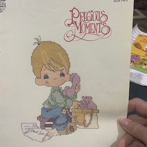May include: Cross stitch pattern featuring a young boy with blonde hair talking on a rotary phone. The pattern is titled "Dear Jon" and is from the Precious Moments book PM-3.