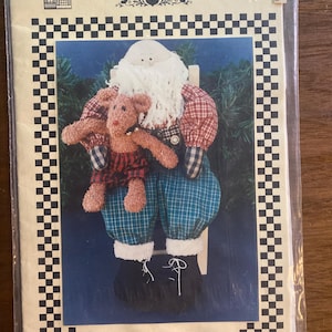 May include: A Vanilla House sewing pattern #39 titled In the Nic of Time for a 14 inch Santa doll. The package features a photo of a fabric Santa with a white beard, red plaid sleeves, and teal plaid pants, holding a small brown teddy bear.