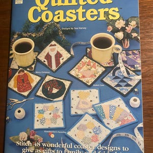 May include: A book titled "Quilted Coasters" with designs by Sue Harvey. The book features 48 different coaster designs, including a Christmas design, a basket case design, and a grandmother's favorites design. The book is on a blue background with a variety of quilting supplies.