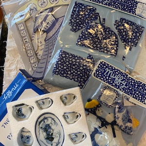 May include: A collection of blue and white miniature tea sets and decorative items, including a tea set with a teapot, cups, and a serving plate. Other items include a blue and white patterned coin purse and a decorative bear. The packaging reads "The Miffy Collection".