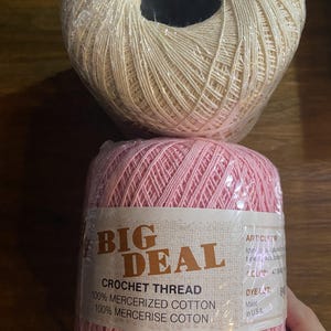 May include: Two balls of Big Deal crochet thread, one cream and one pink, wrapped in clear plastic. The pink ball features a label reading Big Deal Crochet Thread, 100% mercerized cotton, 100% mercerise coton, with additional text and dye lot info.