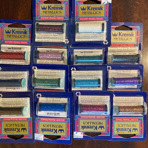 May include: A collection of 10 spools of Kreinik metallic embroidery floss in various colors, including red, blue, green, gold, and silver. Each spool is labeled "Kreinik Metallics" and includes threading instructions.