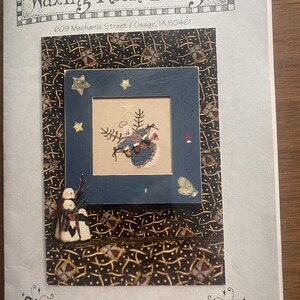 May include: A cross-stitch pattern booklet titled Waxing Moon Designs Lost Mitten Angel #012. The cover features a blue framed cross-stitch of an angel with mittens, set against a black background with gold patterns and small snowman figures.