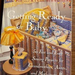 May include: Book cover with a yellow, blue, and red crib with a yellow lamp and a tissue box. The title of the book is "Getting Ready for Baby" and the subtitle is "50 Fast and Easy Sewing Projects for Grandmothers, Aunts, and Mothers-to-Be".