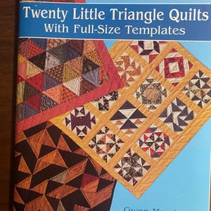May include: A book titled "Twenty Little Triangle Quilts With Full-Size Templates" by Gwen Marston and Pat Holly. The cover displays colourful quilt block designs in various patterns and colours, including red, orange, and brown.