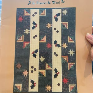 以下が含まれることがあります： クリスマスツリーのデザインが施されたキルトパターンのある本の表紙。タイトルは「Down Home Country Christmas」、サブタイトルは「In Flannel & Wool」。この本はLiberty Homesteadによって出版されています。