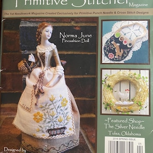 Op de afbeelding: De cover van het tijdschrift "Punch Needle & Primitive Stitcher" toont een pop en borduurprojecten. De pop, "Norma June Pincushion Doll", draagt een crème en tan jurk met een bloemen schort. Andere afbeeldingen zijn onder meer een borduurtas en een krans.