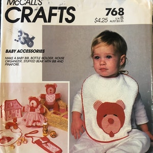 Könnte beinhalten: Ein Nähmuster für Babyzubehör, darunter eine Lätzchen, ein Flaschenhalter, ein Hausorganisator und ein Stofftier mit Lätzchen und Latzhose. Das Muster ist von McCall's Crafts und trägt die Nummer 768. Das Muster kostet 4,25 $.