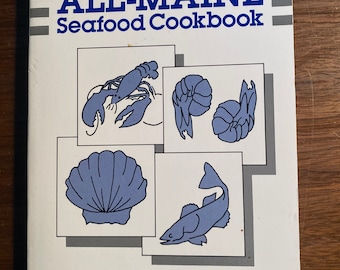 May include: A white book cover with the title "ALL-MAINE Seafood Cookbook" in blue and black text. The cover features illustrations of a lobster, clams, and a fish.