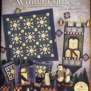May include: A book cover featuring a winter theme with penguins, snowflakes, and quilted creations. The title of the book is "Winter Follies" and the author is Debbie Mumm. The book cover also includes the text "Playful penguins and shimmering snowflakes take center stage in this collection of quilted creations."