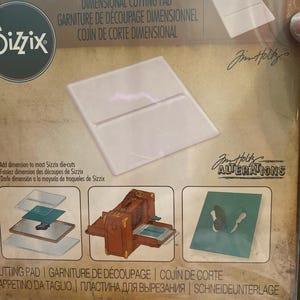 May include: A Sizzix dimensional cutting pad in a clear plastic package. The package includes the text "DIMENSIONAL CUTTING PAD" and "ALTERATIONS" by Jim Holtz. The pad is designed to add dimension to Sizzix die-cuts.