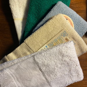 Puede incluir: Colecci&oacute;n de toallitas plegadas en varios colores: blanco, verde, azul claro y crema. Las toallitas est&aacute;n hechas de una tela texturizada, con una etiqueta visible en una de ellas. Las toallitas est&aacute;n dispuestas en forma de abanico.