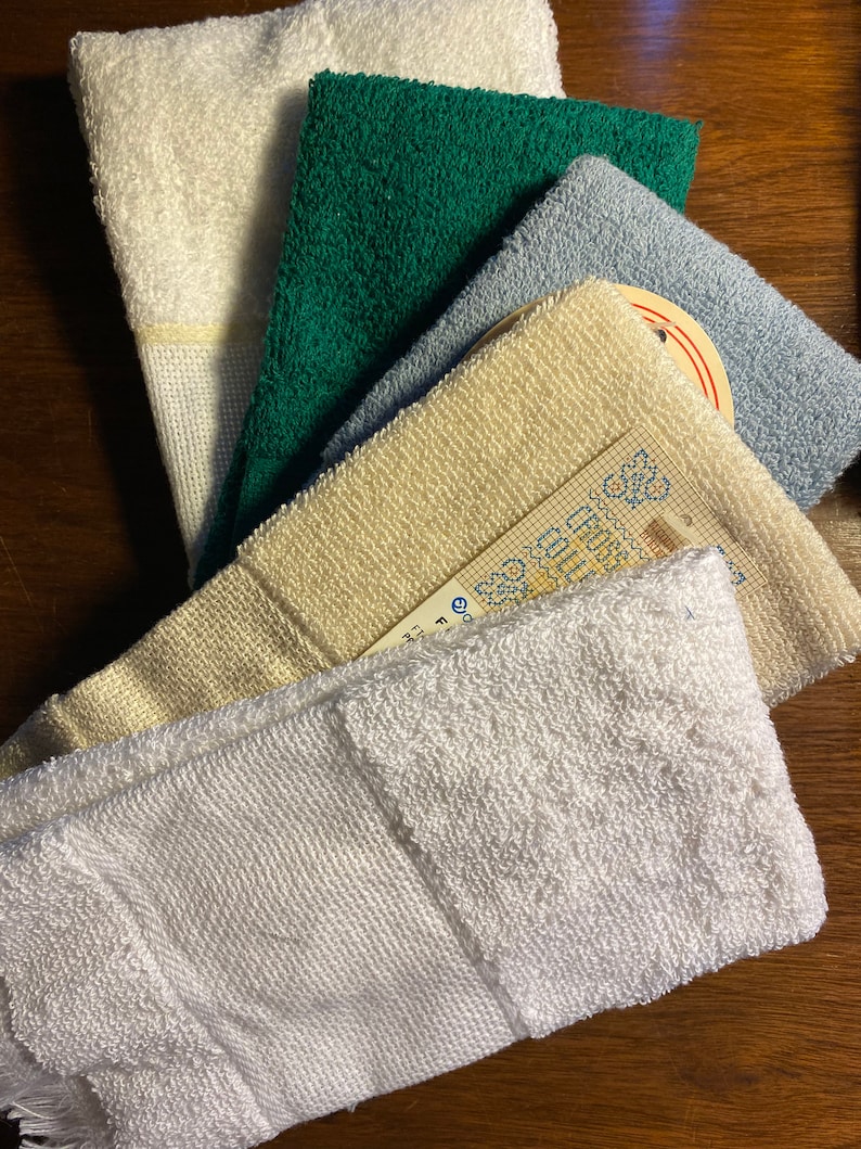 Puede incluir: Colecci&oacute;n de toallitas plegadas en varios colores: blanco, verde, azul claro y crema. Las toallitas est&aacute;n hechas de una tela texturizada, con una etiqueta visible en una de ellas. Las toallitas est&aacute;n dispuestas en forma de abanico.