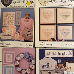May include: Four different HeartStrings cross-stitch patterns. The first pattern is a collection of alphabet monograms. The second pattern is a collection of four heart-shaped designs. The third pattern is a wreath with a bird and a heart. The fourth pattern is a collection of cat-themed designs.