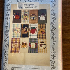 May include: A pattern for tea towel embroidery featuring a variety of teapots with different designs, including a snowman, a house, a pumpkin, a rooster, and a strawberry. The pattern is titled "Tea Time Tea Towels" and is from Becky's Ivy Cottage.