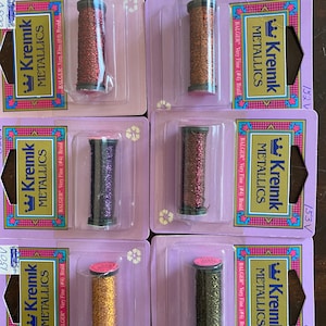 May include: Six spools of Kreinik metallic embroidery floss in various colors, including copper, gold, purple, and green. Each spool is labeled "Kreinik Metallics" and "Balger Very Fine (#4) Braid".