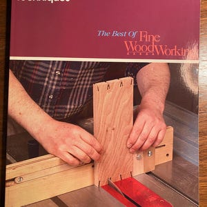 May include: A book titled "Joinery Techniques: The Best of Fine Woodworking" with a photo of a person using a table saw to cut a piece of wood.