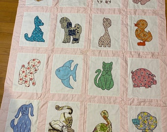 Könnte beinhalten: Eine rosafarbene und weiße Patchwork-Decke mit verschiedenen Tier-Applikationen. Die Decke zeigt eine Vielzahl von Tieren, darunter einen Vogel, eine Katze, einen Hund, eine Ente, einen Fisch, ein Schwein, eine Schildkröte und einen Elefanten. Die Decke ist aus verschiedenen Stoffen und Farben gefertigt.