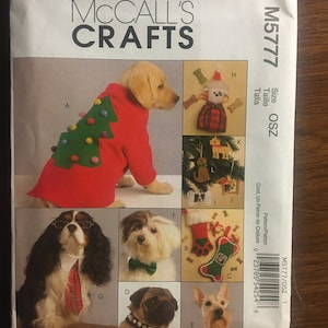 May include: McCall's Crafts sewing pattern M5777/OSZ for making dog clothes. The pattern includes five different designs for holiday outfits, including a Christmas tree sweater, a bow tie, a stocking, and a Santa hat. The pattern is printed on white paper with black text and illustrations.