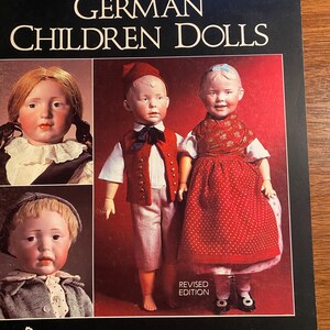 May include: A book cover featuring a title that reads "German Children Dolls" with a revised edition note. The cover features four antique dolls in various poses and clothing. The book is published by Scott Publications.