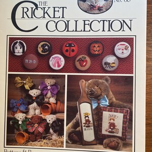 May include: A cross-stitch pattern booklet featuring a collection of teddy bear designs. The cover features a cross-eyed teddy bear wearing a bow tie and holding a book. The title of the booklet is "The Cricket Collection" and the number "68" is printed on the cover. The booklet includes a variety of designs, including a teddy bear with a bow tie, a teddy bear with a bow, and a teddy bear with a book. The booklet also includes a variety of buttons and bows.