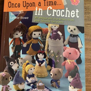 May include: A softcover book titled Once Upon a Time... in Crochet by Lynne Rowe, featuring 30 amigurumi characters from fairytales. The cover displays various crocheted figures including a princess, a tower, a pig, and gnomes on a blue background.