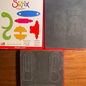 Puede incluir: Un juego de troqueles Sizzix Originals para manualidades. El juego de troqueles incluye una variedad de formas, incluyendo un gancho, un pestillo y un elemento decorativo. El juego de troqueles está diseñado por Emily Humble y está hecho en los Estados Unidos. El juego de troqueles es 655000 y se muestra al 100% de su tamaño real.