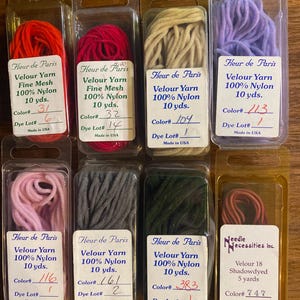 May include: Eight clear plastic blister packs containing various colors of velour yarn. Seven packs are labeled Fleur de Paris, 100% nylon, 10 yds. One pack is labeled Needle Necessities, velour 18 shadowdyed, 5 yards. Colors include red, pink, beige, purple, gray, and dark green.