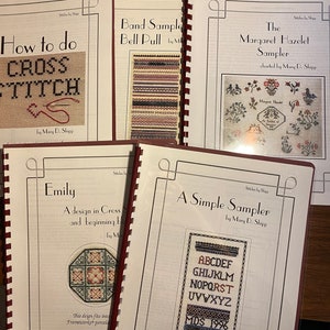 Könnte beinhalten: Fünf Kreuzstich-Musterbücher mit bunten Umschlägen. Die Titel lauten "How to do Cross Stitch", "Band Sample Bell Pull", "The Margaret Hazelet Sampler", "Emily" und "A Simple Sampler".